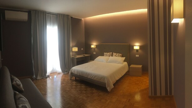 A hotel room with a bed, nightstands, a sofa, and a window with curtains. - Robin Rooms (Montegranaro)