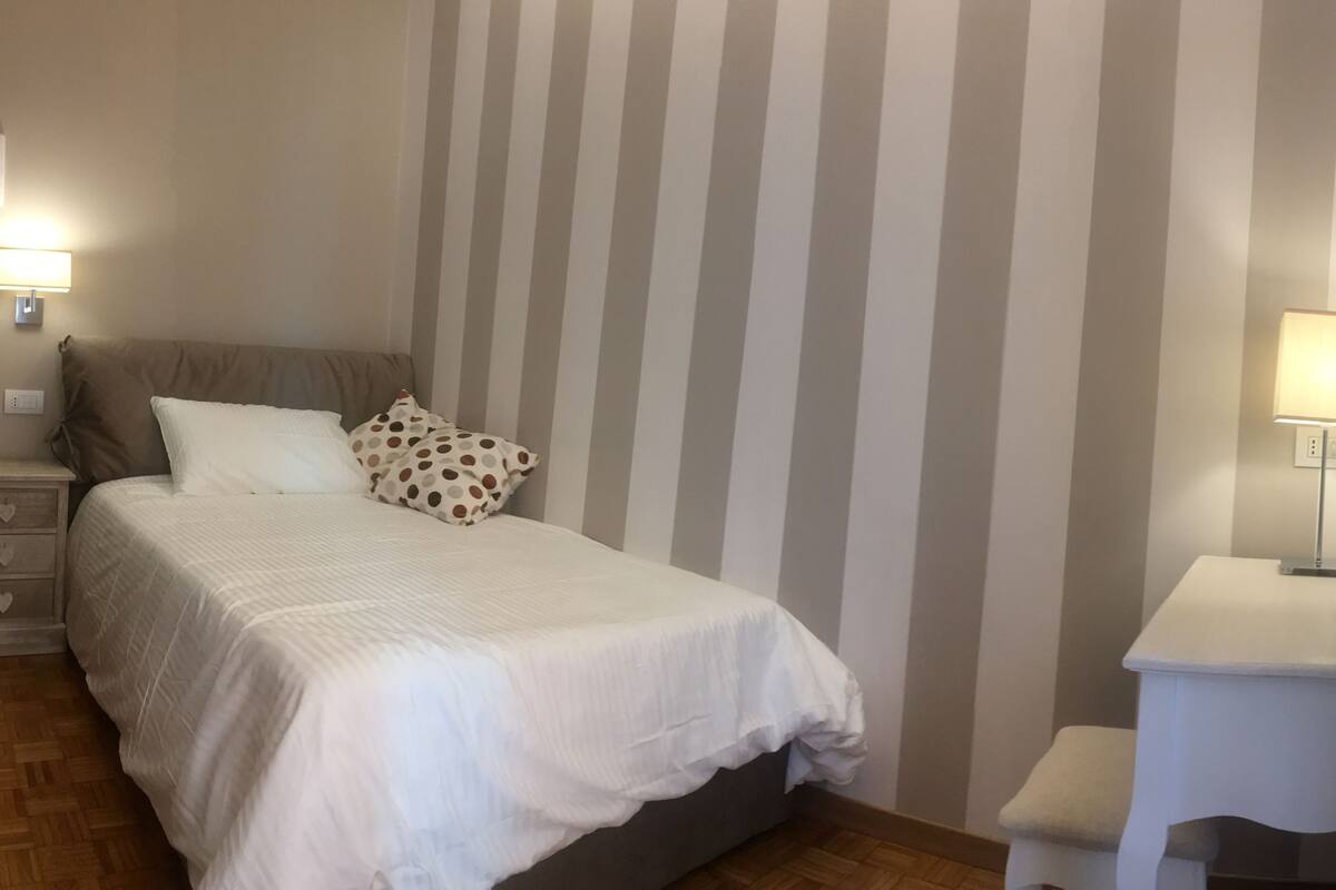 A neatly arranged bedroom with a bed, a bedside table, a lamp, and a striped wall.