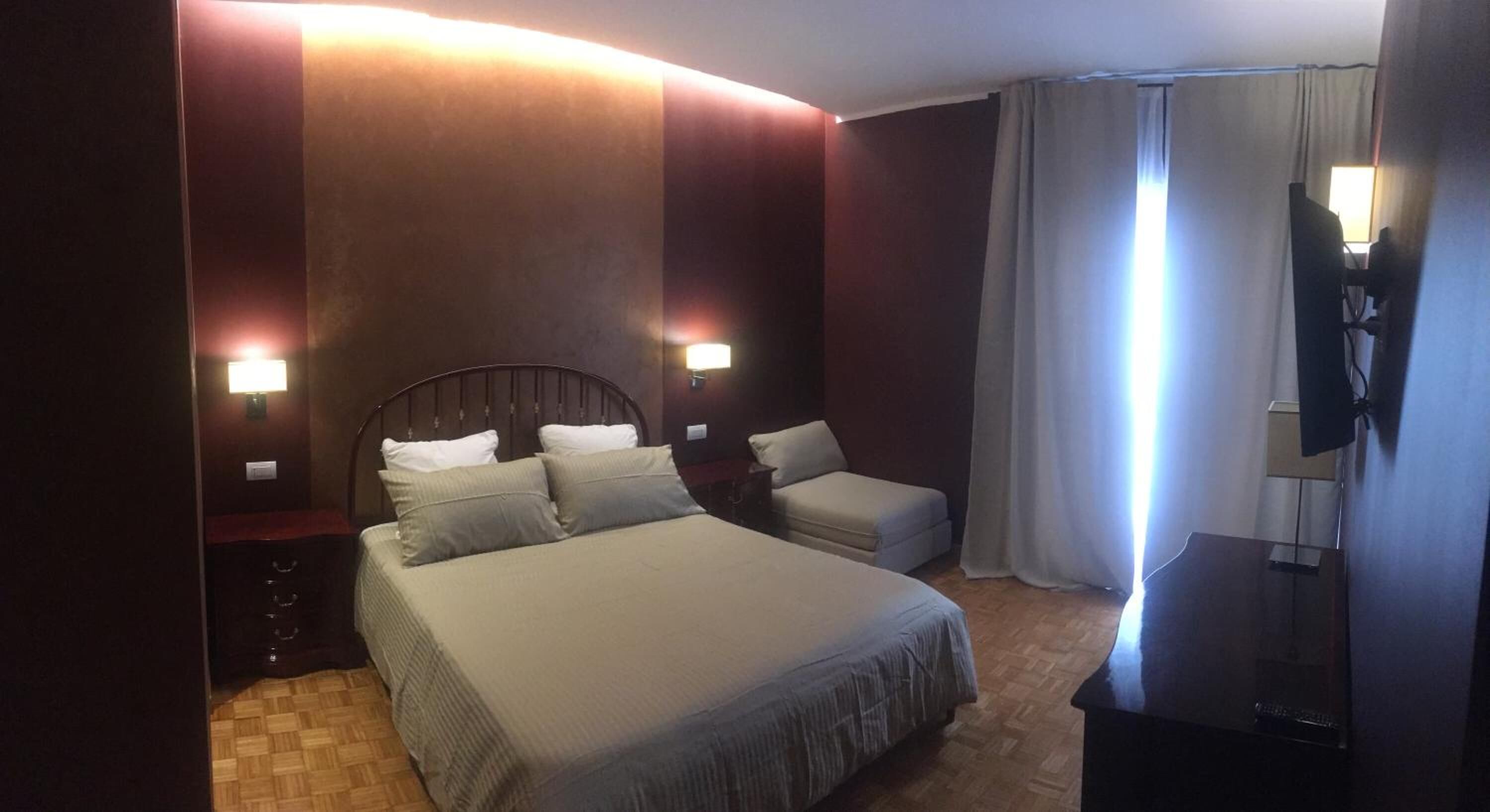 Hotellihuone, jossa on suuri sänky, pienempi sohva, työpöytä tuolilla, televisio ja ikkuna, jossa on verhot.