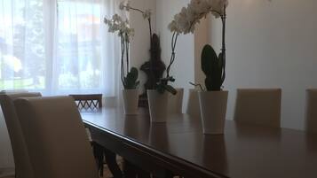 A dining area with a wooden table, white chairs, and potted orchids.