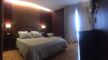 A hotel room with a large bed, two wall-mounted lamps, a wooden floor, and a TV on the right side.