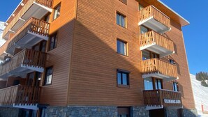 A multi-story wooden building with balconies, stone base, and a clear sky. - Apartment 6 pax, Mont Blanc view, near slopes, parking (La Plagne)