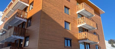 A multi-story wooden building with balconies, stone base, and a clear sky.