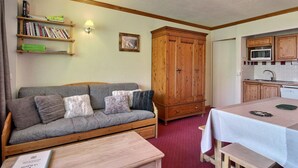 A cozy room with a grey sofa, wooden cabinet, and a small kitchen area with a microwave. - Apartment 6 pax, Mont Blanc view, near slopes, parking (La Plagne)