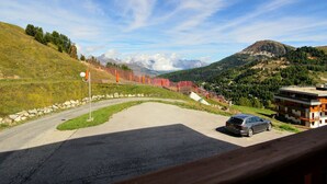 A parking area with a car, a building with balconies, and a mountainous landscape in the background. - Apartment 6 pax, Mont Blanc view, near slopes, parking (La Plagne)