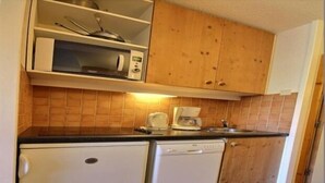 Una cocina compacta con armarios de madera, microondas, cafetera y lavavajillas.