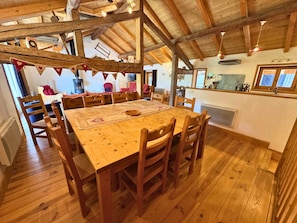 Un comedor rústico con una mesa y sillas de madera, una cocina al fondo y una chimenea de piedra.