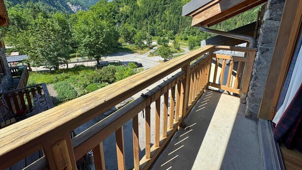 A wooden balcony with a view of a mountainous landscape and a parking area.