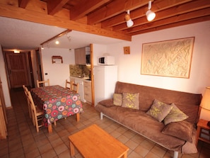 A cozy living room with a brown sofa, a wooden coffee table, and a dining area with a colorful tablecloth.