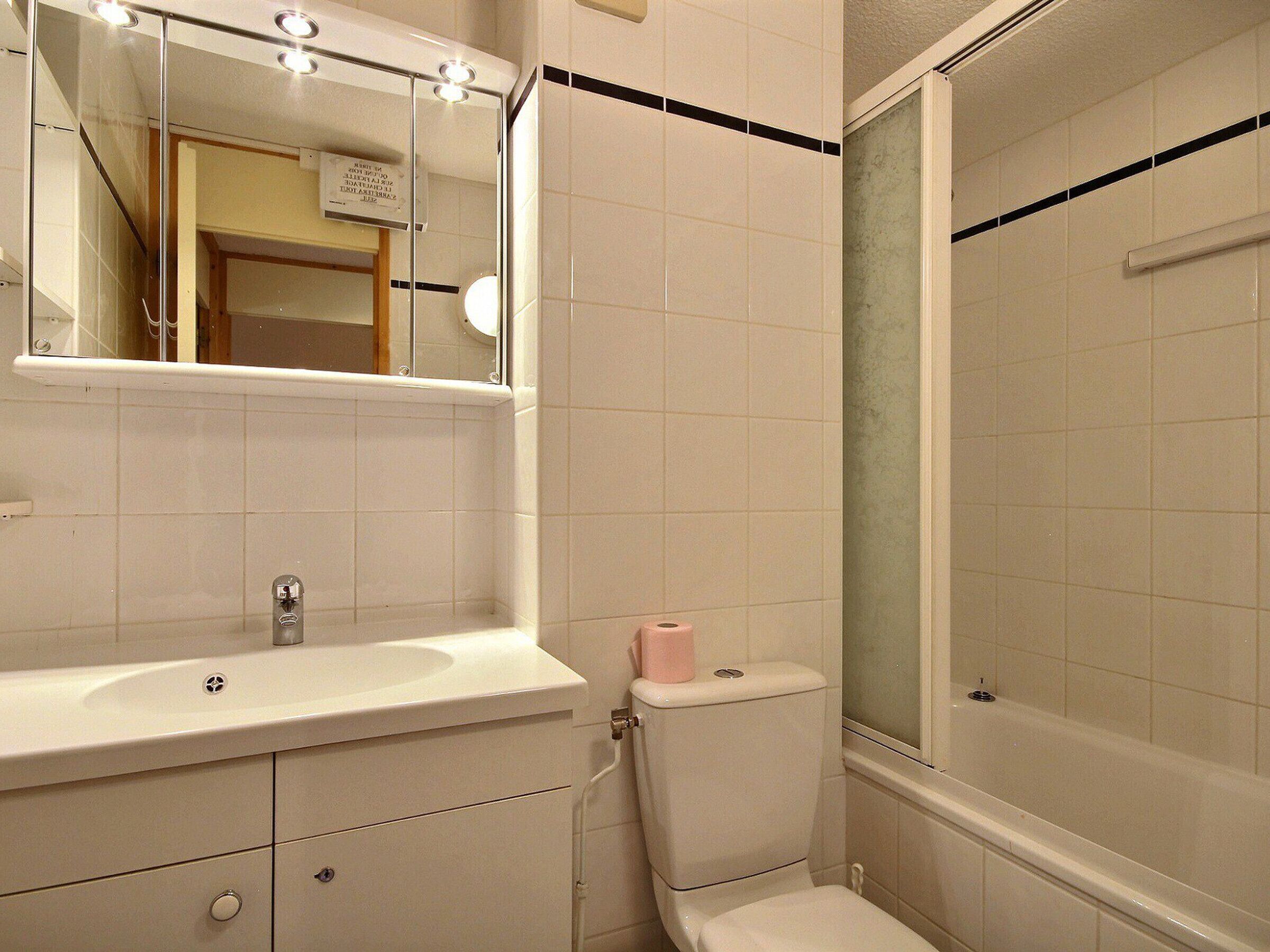 A bathroom with a white sink, mirror, toilet, and a glass-enclosed shower area.