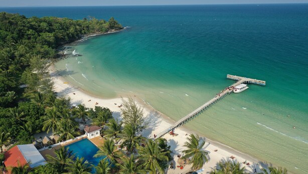 An aerial view of a beach with a pier extending into the ocean, surrounded by lush greenery and a clear blue sea. - Sunrise Vuth Resort (Koh Rong)