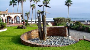 Ein angelegter Garten mit einer zentralen Ziegelstruktur, Palmen und Blick aufs Meer.