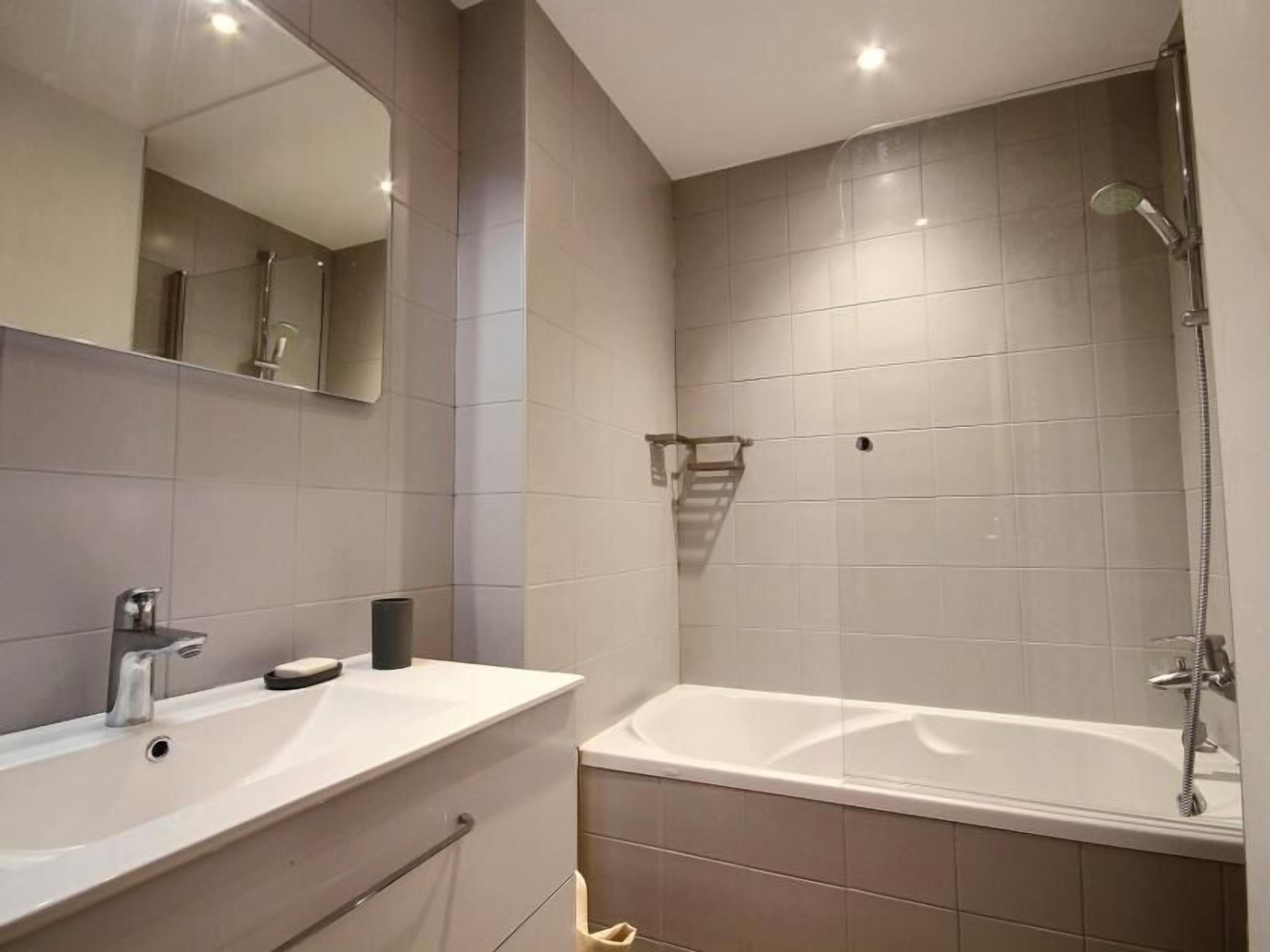 A modern bathroom with a large mirror, a sink, and a bathtub.