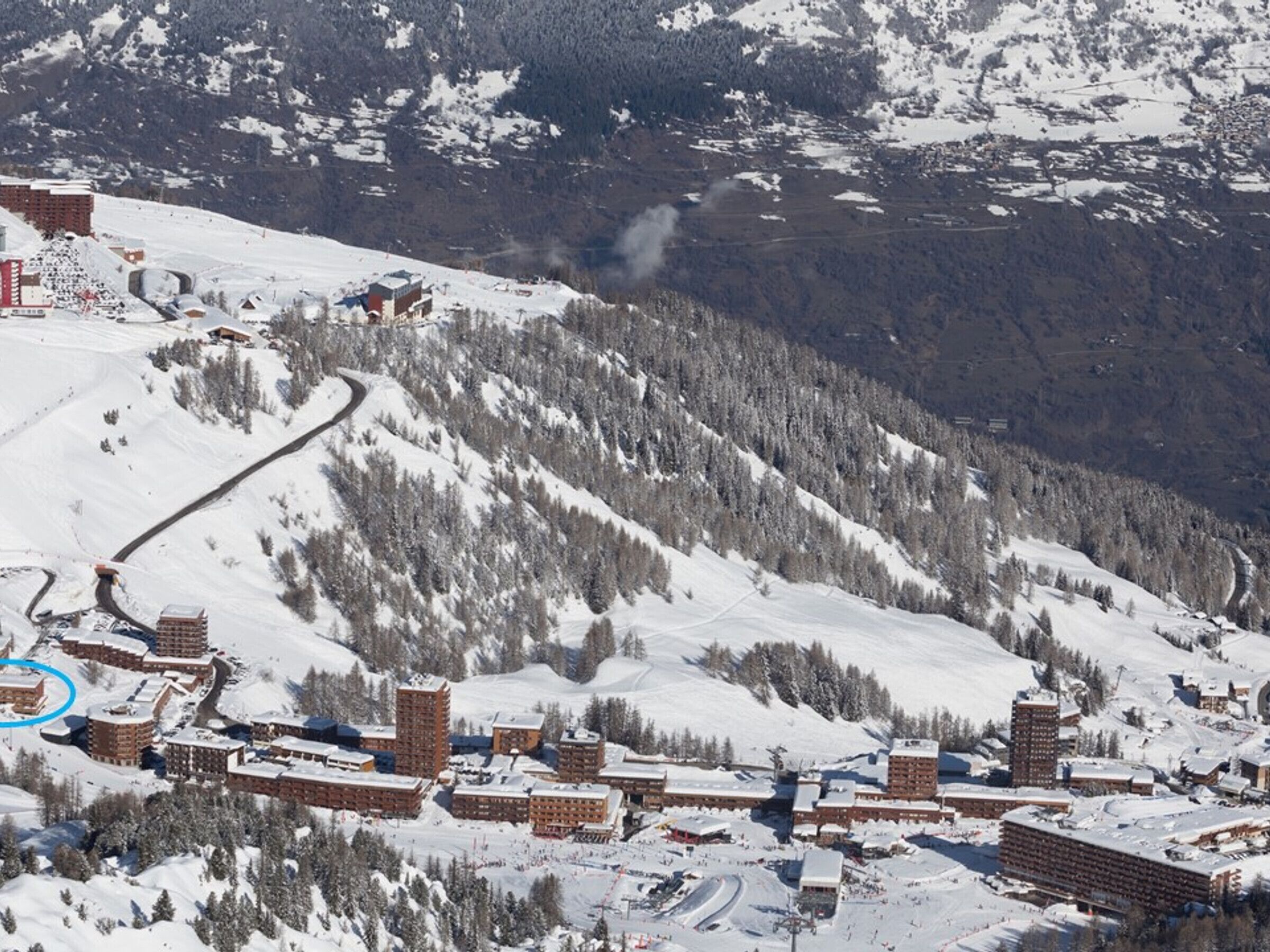 Une station de ski enneigée comprenant plusieurs bâtiments, dont un grand hôtel doté d’une cour centrale et de plusieurs structures plus petites.