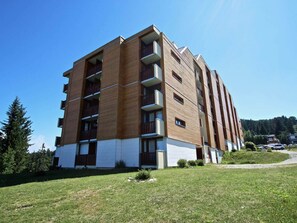 A multi-story residential building with balconies, a flat roof, and a grassy front yard.