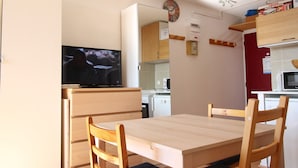 Kompakti keittiö, jossa on ruokapöytä ja -tuolit, televisio ja mikroaaltouuni.
