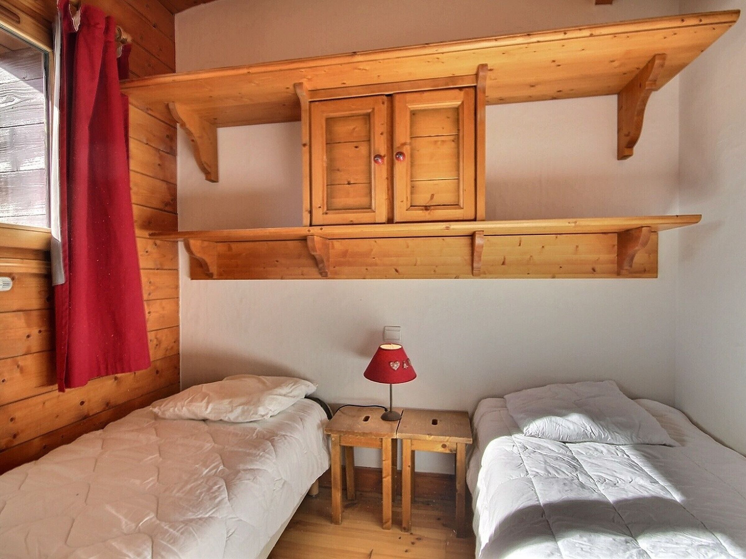 Een houten kamer met twee bedden, een kleine tafel met een lamp en een houten kastje boven de bedden.