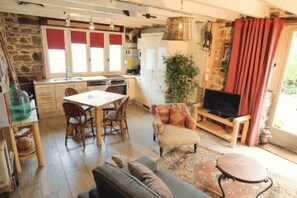A cozy living area with a dining table, chairs, a sofa, a television, and a large plant.