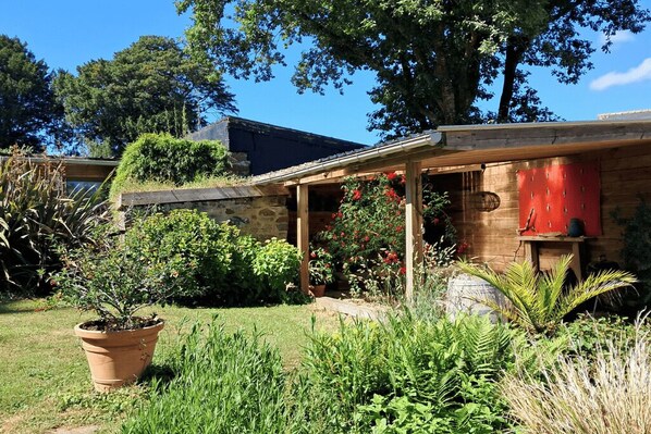 A house with a covered porch, a stone wall, and a garden with various plants and a potted plant.