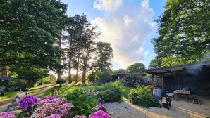 Un jardín con camino de grava, flores de hortensia y una zona de barbacoa.