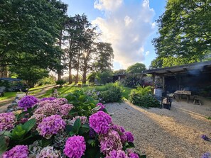 Un jardin avec un chemin de gravier, des hortensias et un espace barbecue.