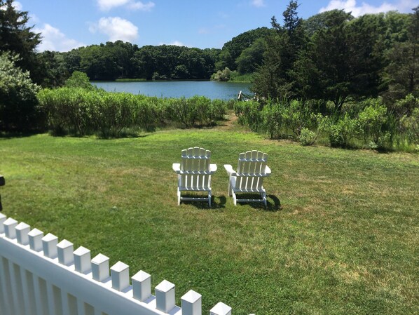 Zwei Adirondack-Stühle, die auf einen See blicken, mit einem bewaldeten Hügel im Hintergrund.