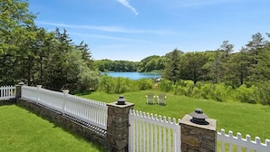 Une pelouse bien entretenue, bordée d’un muret en pierre et d’une clôture blanche, un ciel bleu dégagé et un lac en arrière-plan.