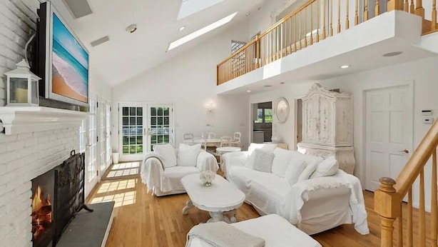 Un salon spacieux doté d’une cheminée, de meubles blancs et d’un balcon avec une balustrade en bois.