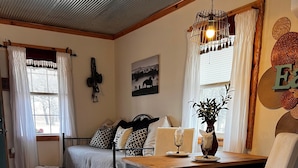 Une pièce confortable avec un lit, une table à manger entourée de chaises, un luminaire suspendu et un tableau au mur.