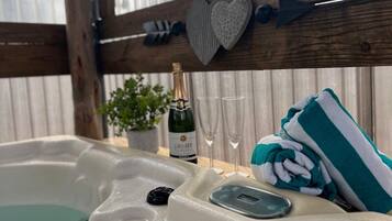 Un bain à remous avec une structure en bois, des décorations en forme de cœur, une bouteille de champagne, des verres et une serviette.