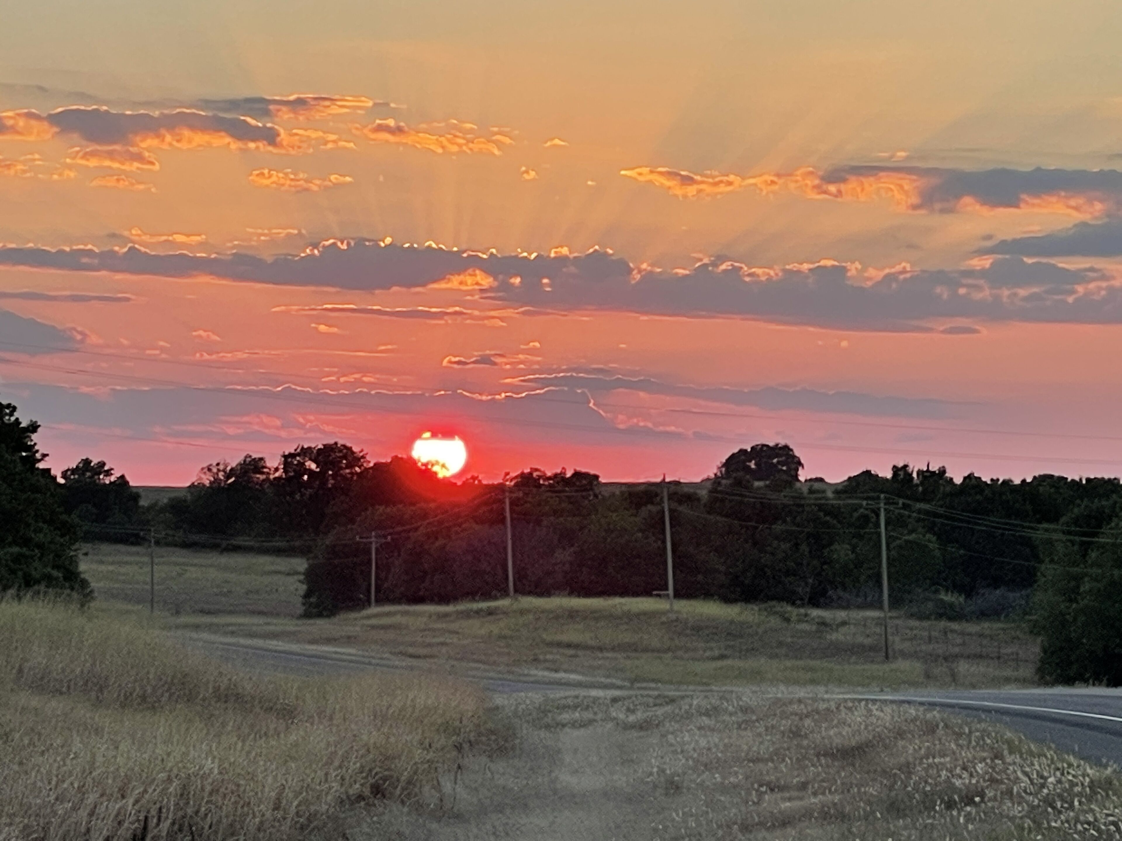 Un atardecer sobre un paisaje rural con una carretera y árboles.
