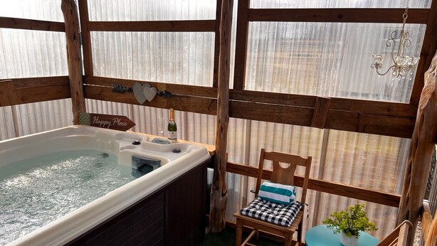 Un bain à remous avec une bouteille de champagne, une chaise avec un coussin à carreaux et une petite table avec une plante.