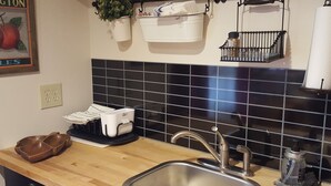 Eine Küche mit Spüle, einer Holzausziehtafel, einer schwarzen Fliesenwand, einer hängenden Pflanze und einem Metalldrehregal.