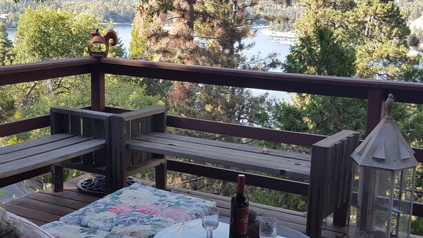 Eine Holzterrasse mit einem Glastisch, zwei Stühlen, einer Bank und einem Laternenleuchter.