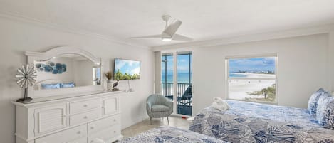 Ein Schlafzimmer mit zwei Betten, einem Schminktisch, einem Stuhl, einem Deckenventilator und einem Balkon mit Meerblick.