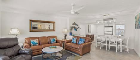 A living room with a brown leather sofa, a black leather armchair, a round coffee table, and a ceiling fan.