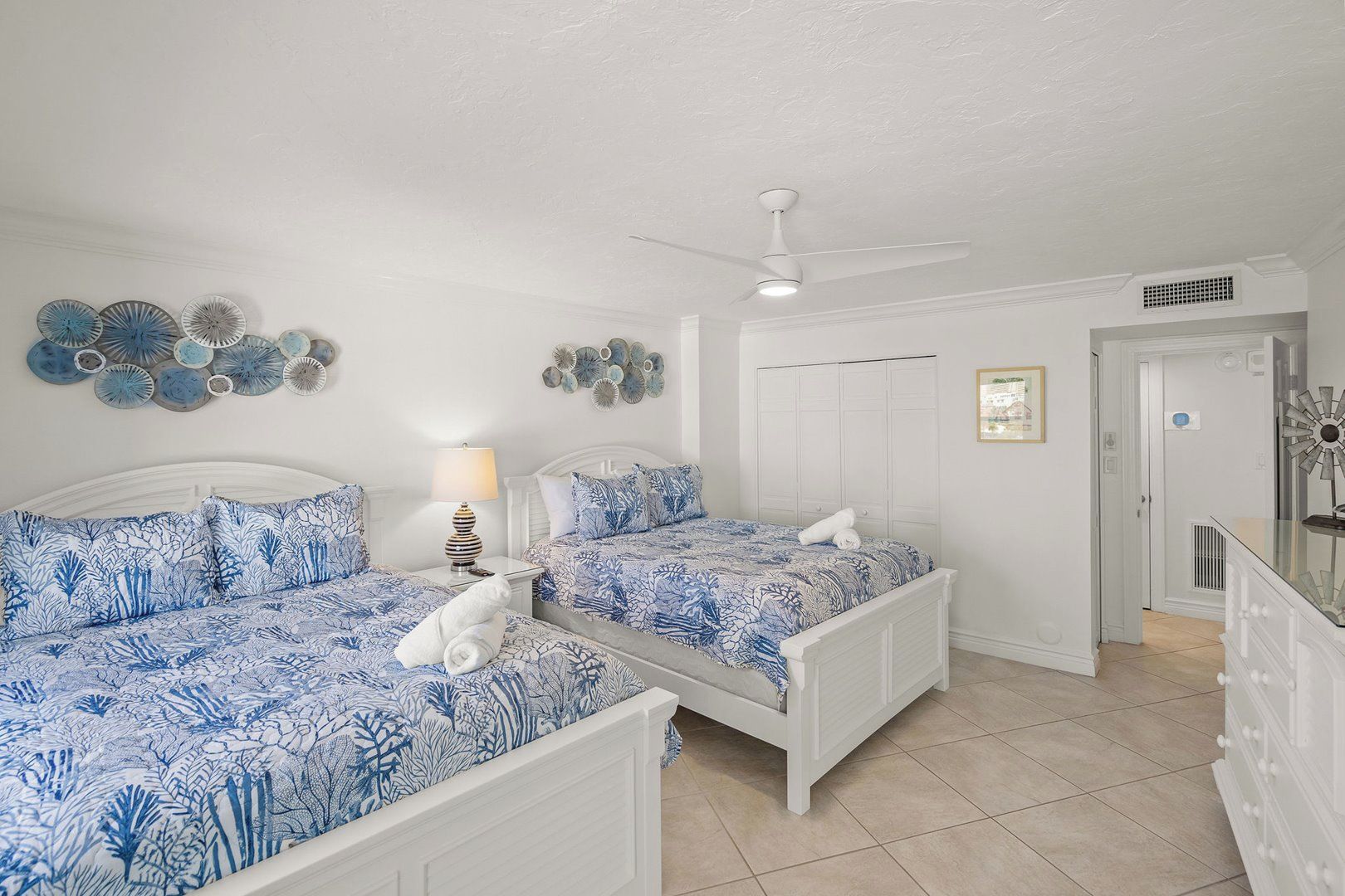 A bedroom with two beds, a ceiling fan, decorative wall art, and a door leading to another room.