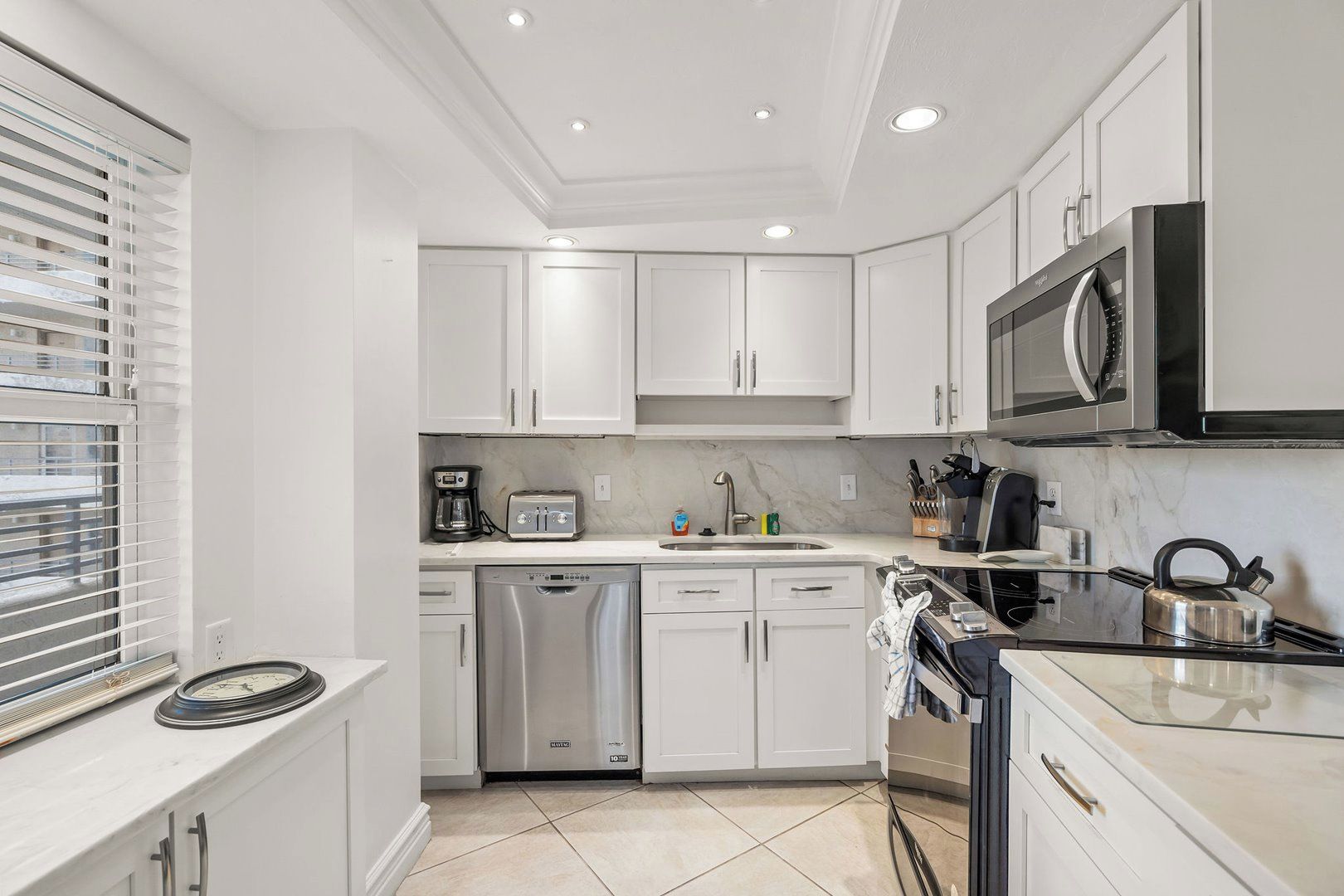 A modern kitchen with white cabinetry, a built-in microwave, a dishwasher, and a stove.