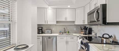 Una cocina moderna con armarios blancos, microondas integrado, lavavajillas y estufa.