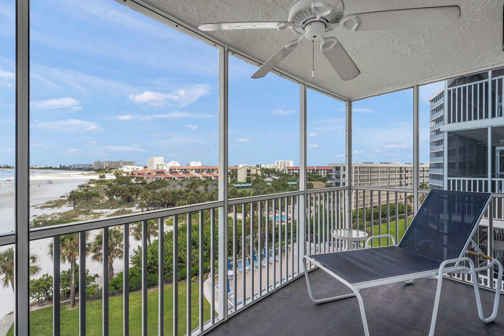 Un balcon avec vue sur la plage et la ville, un ventilateur de plafond et un coin salon avec une table et des chaises.