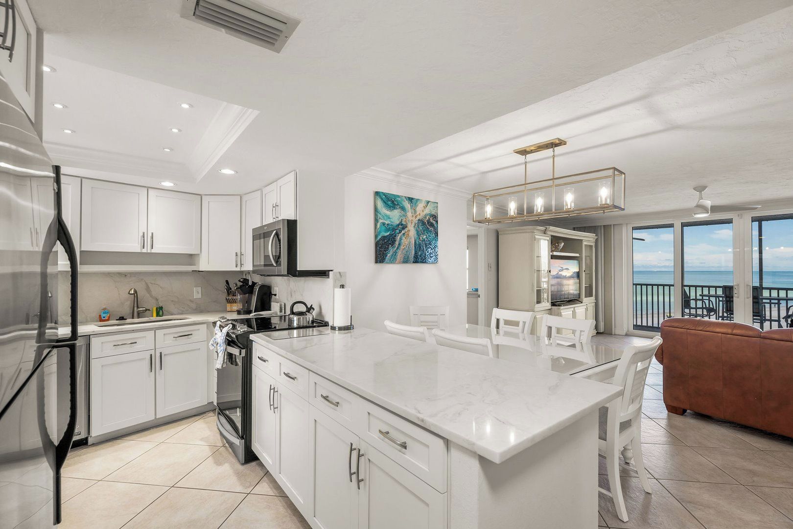 A modern kitchen with white cabinetry, a large island, and a dining area with a view of the ocean.