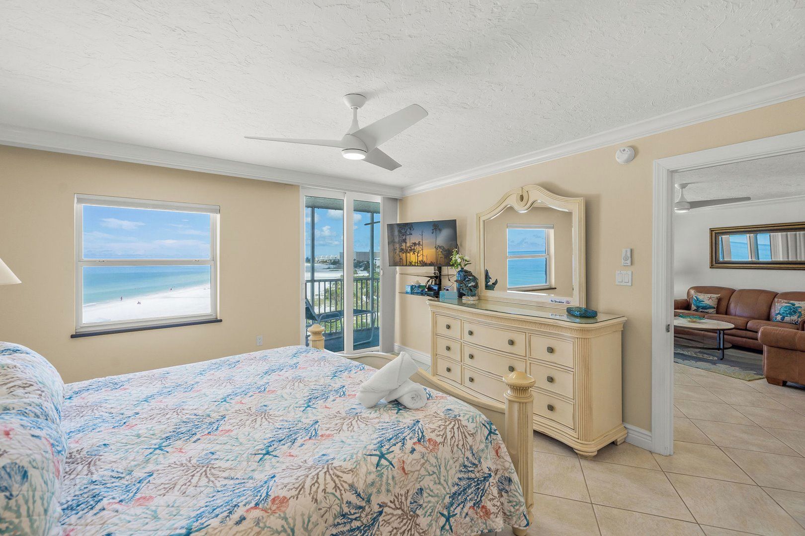 A bedroom with a bed, dresser, and a view of the beach.