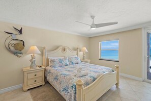 Une chambre à coucher comprenant un lit, deux tables de chevet avec des lampes, un ventilateur de plafond, un élément décoratif mural et une fenêtre avec vue.