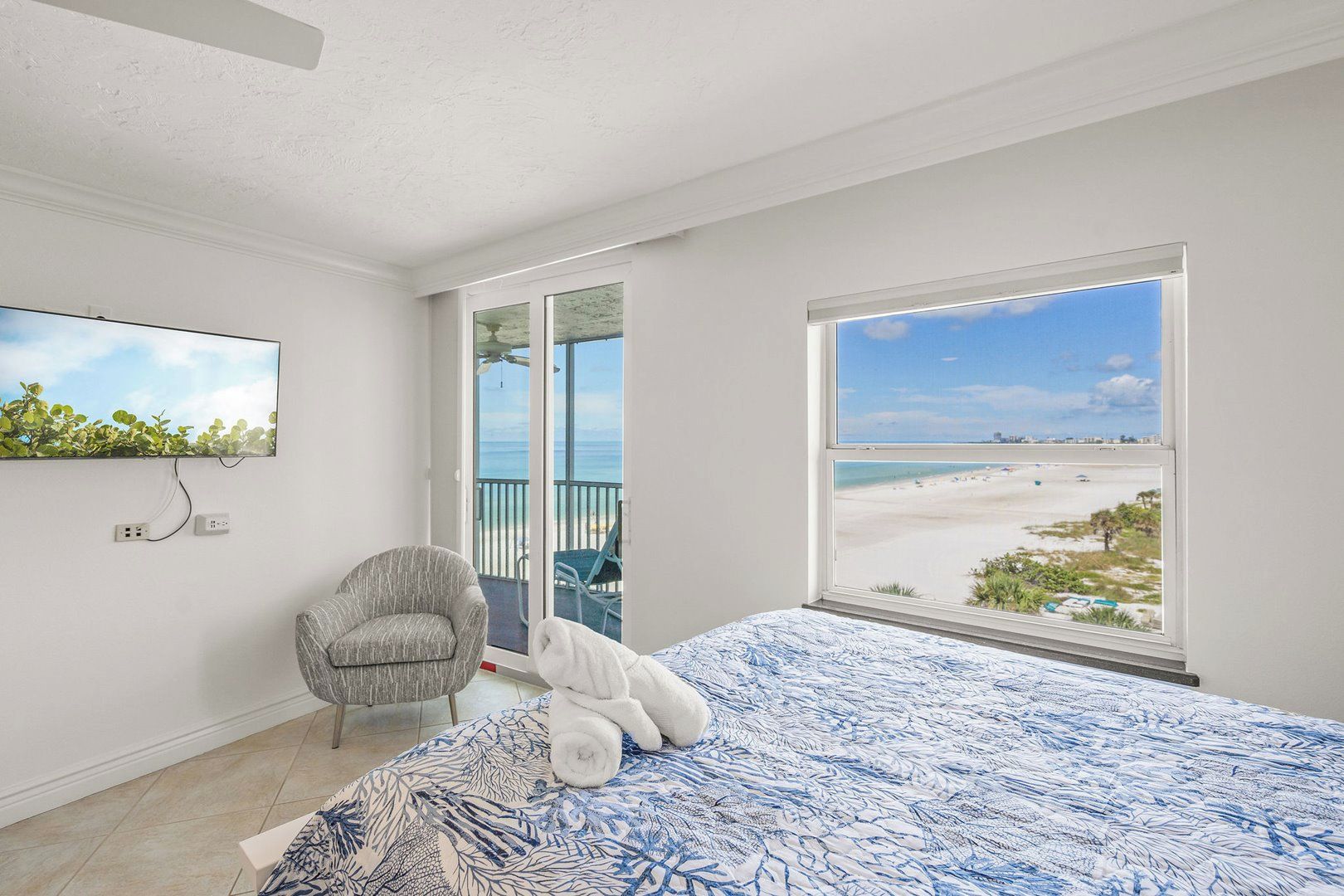 Een slaapkamer met een groot bed, een stoel, een televisie en een balkon met uitzicht op het strand.