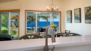 A kitchen with a view of the ocean, a chandelier, and framed artwork on the wall.