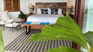 A bedroom with a bed, bedside lamps, a potted plant, a chair, and a large window.