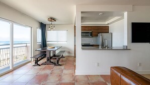 Une cuisine moderne dotée d’un four à micro-ondes et d’un réfrigérateur intégrés, un coin repas avec un banc, et de grandes fenêtres offrant une vue sur la plage.