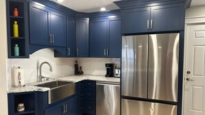 Een keuken met donkerblauwe kastjes, roestvrijstalen apparatuur en een marmeren aanrecht.