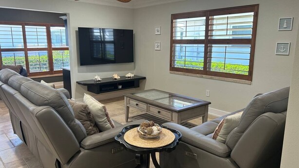 Een woonkamer met een grote hoekbank, een glazen salontafel en een flatscreen televisie aan de muur.