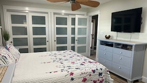Een slaapkamer met een bed, een dressoir, een televisietoestel en een plafondventilator.